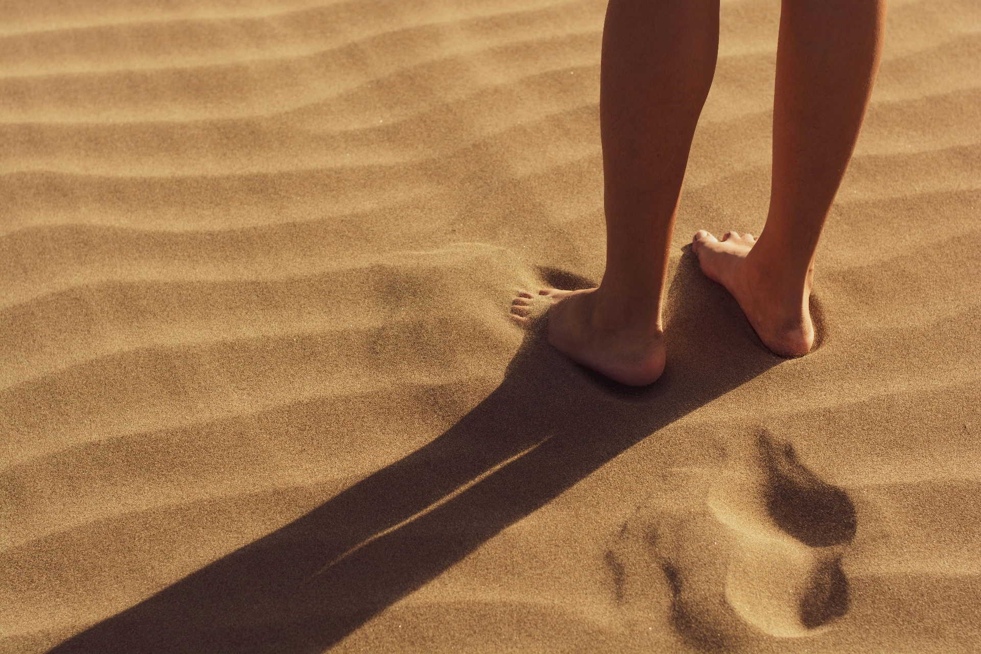 Bare feet walking on warm sand dunes in golden light